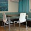 Una sala da pranzo con tavolo, due sedie bianche, divano angolare e tende azzurre.