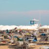 Spiaggia affollata con molti ombrelloni bianchi.