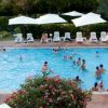 Piscina affollata con ombrelloni bianchi e rigogliosi cespugli fioriti.