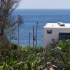 Camper bianco vicino al mare, circondato da vegetazione.