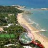 Vista aerea di una spiaggia con vegetazione e mare. Testo 