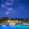 Piscina illuminata di sera, circondata da piante e un cielo blu scuro.
