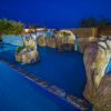 Piscina illuminata di sera con grandi rocce decorative e piante.