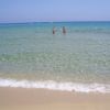 Una spiaggia sabbiosa con mare limpido, due persone camminano in acqua.