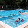 Persone nuotano e giocano con palloni in una piscina all'aperto.