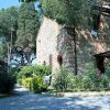 Edificio in pietra con alberi e arbusti circostanti, strada di ghiaia.