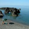 Rocce imponenti in mare con una spiaggia tranquilla, un ombrellone e una persona seduta.