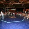Persone sedute in cerchio attorno a una pista di ballo blu sotto un tetto di legno.