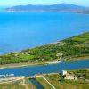 Vista aerea di una costa con mare blu e vegetazione verde.
