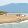 Spiaggia sabbiosa con bagnanti, alberi e colline sullo sfondo.