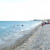 Spiaggia ghiaiosa con bagnanti e mare calmo.