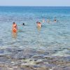 Persone che nuotano in mare limpido con fondo roccioso.