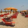 Una spiaggia con ombrelloni arancioni e lettini. Persone rilassate sotto il sole. Atmosfera estiva.