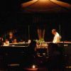 Persona dietro un bancone in un bar all'aperto, atmosfera serale con luci soffuse.