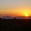Un tramonto su un paesaggio con silhouette di colline e un cielo arancione.
