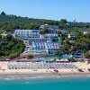 Spiaggia affollata con ombrelloni, mare e colline sullo sfondo.