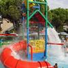 Gioco d'acqua colorato con scivolo rosso e getti d'acqua. Bambini giocano nella piscina sottostante.