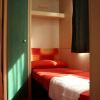 Una piccola stanza con letto singolo, lenzuola rosse e armadio verde chiaro.
