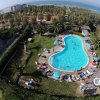 Piscina a forma libera con lettini e persone. Vista mare sullo sfondo.
