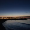 Spiaggia illuminata al crepuscolo con vista su luci cittadine.
