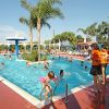 Una piscina all'aperto con persone che nuotano, circondata da palme e lettini.