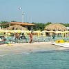 Spiaggia con ombrelloni gialli, lettini, capanne di paglia e una bandiera italiana.
