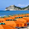 Spiaggia con ombrelloni arancioni e vista su castello su una scogliera.