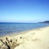 Spiaggia sabbiosa con mare calmo, cielo blu e colline in lontananza.