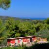 Una casetta rossa immersa nel verde con vista sul mare in lontananza.