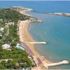 Vista aerea di una spiaggia sabbiosa con ombrelloni e mare azzurro.