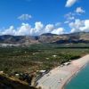 Una lunga spiaggia sabbiosa con ombrelloni, vista panoramica di colline e cielo blu.