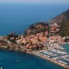 Vista aerea di un borgo costiero con porto, circondato dal mare e colline.
