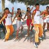 Un gruppo di persone balla sulla spiaggia sotto ombrelloni di paglia.