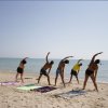 Persone fanno stretching sulla spiaggia vicino al mare.