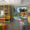 Spazio giochi con struttura in rete, sedili colorati e televisore su mobile giallo.