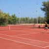 Due persone che giocano a tennis su un campo all'aperto circondato da alberi.