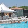 Persone nuotano in una piscina vicino a un'area con sdraio e una tenda bianca.