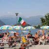 Persone sedute a un bar all'aperto vicino a un lago, con ombrelloni e bandiera italiana.