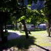 Area campeggio con roulotte, tenda e alberi verdi.