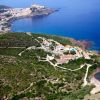 Vista aerea di una costa collinare con un villaggio e un mare blu.