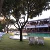 Piscina all'aperto circondata da lettini su prato verde, alberi e un edificio con terrazza.