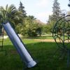 Un parco giochi con scivolo e struttura metallica, circondato da palme e alberi.