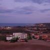 Panorama costiero con mare, edifici e colline al tramonto.