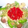 Insalata con fusilli rossi, spaghetti gialli, funghi e peperoni verdi su foglie verdi.