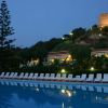Piscina di notte con sedie a sdraio bianche e una collina con edificio illuminato sullo sfondo.