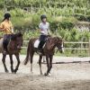 Due persone a cavallo in un'area esterna con recinzione.