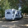Camper bianco parcheggiato all'ombra di alberi, in un ambiente boscoso.