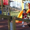 Un bambino gioca sorridente su un'altalena in un parco giochi colorato.