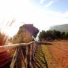 Sentiero sterrato con recinzione in legno, vista panoramica su colline e mare al tramonto.