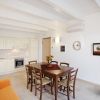 Cucina e sala da pranzo luminosa con tavolo in legno, sedie, cucina bianca e pianta.